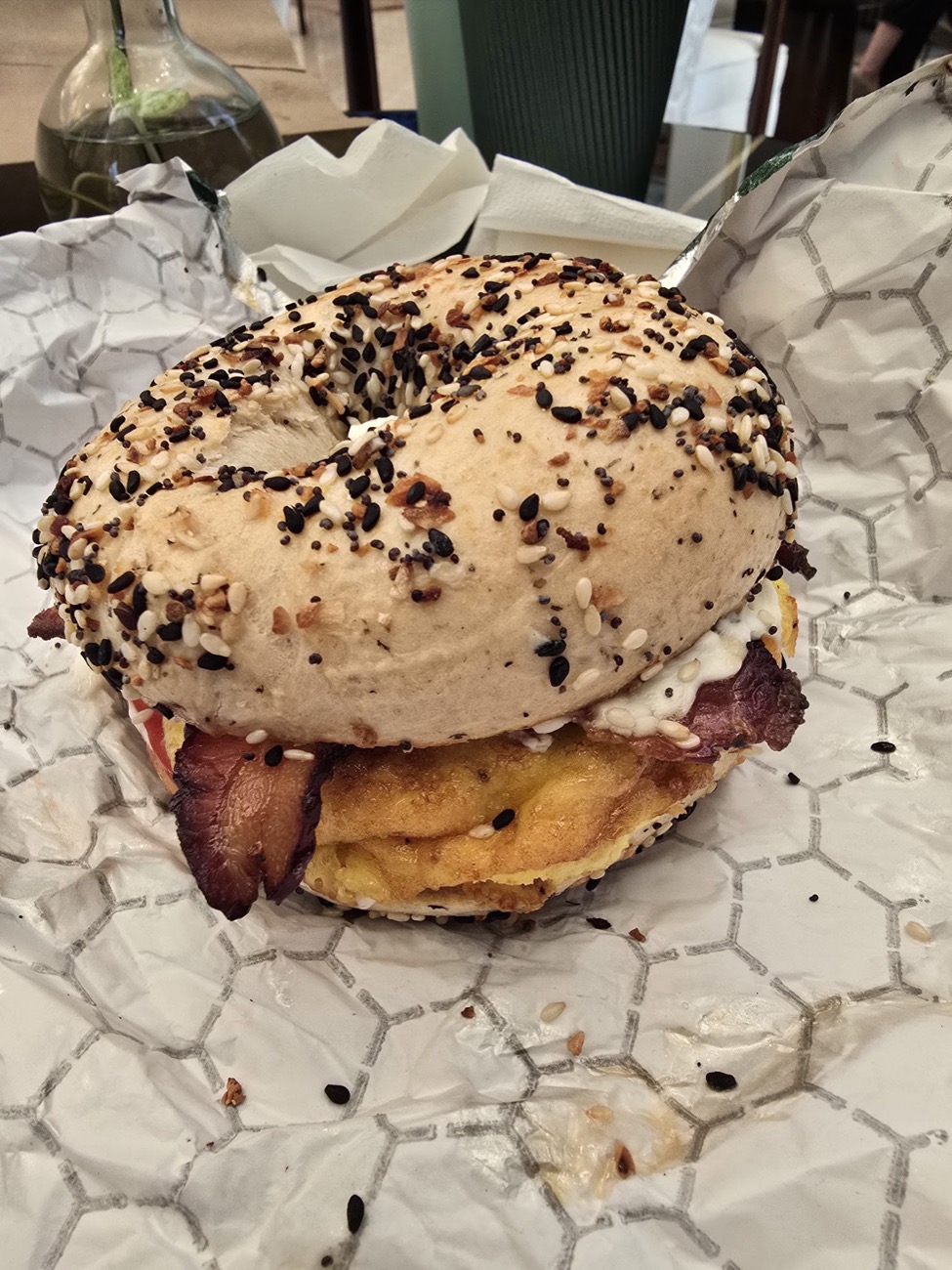 An everything-bagel breakfast sandwich with egg and bacon, wrapped in paper
